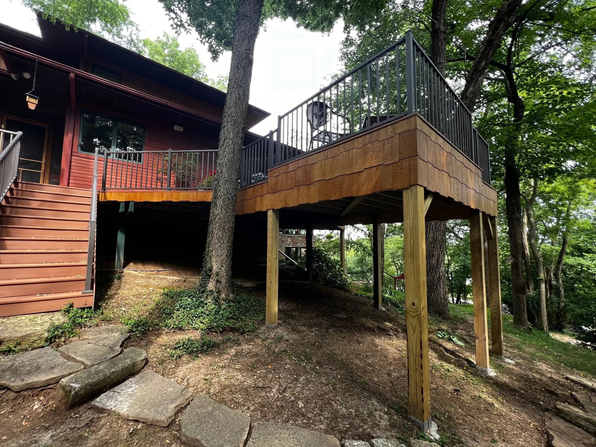 Elevated deck and wood stair against the home, framed by trees