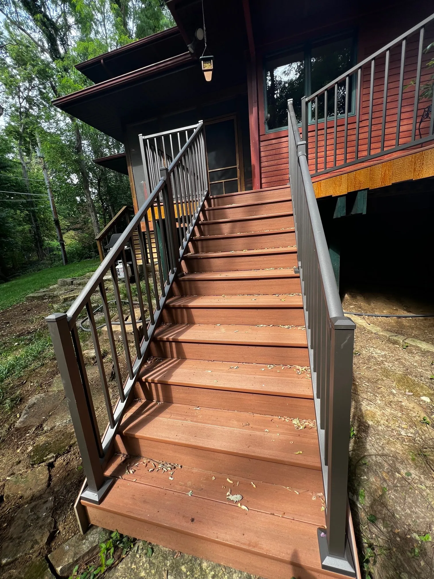 Deck stair with black metal balusters descending the hillside