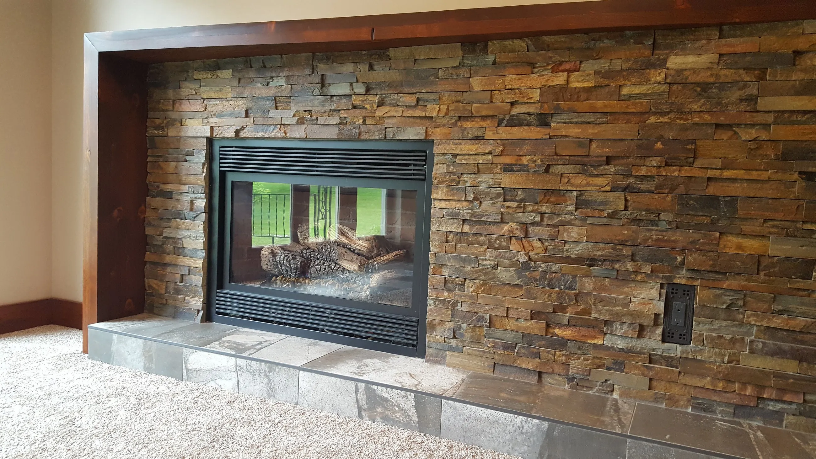 Stacked stone fireplace surround with a wood mantel in a finished basement