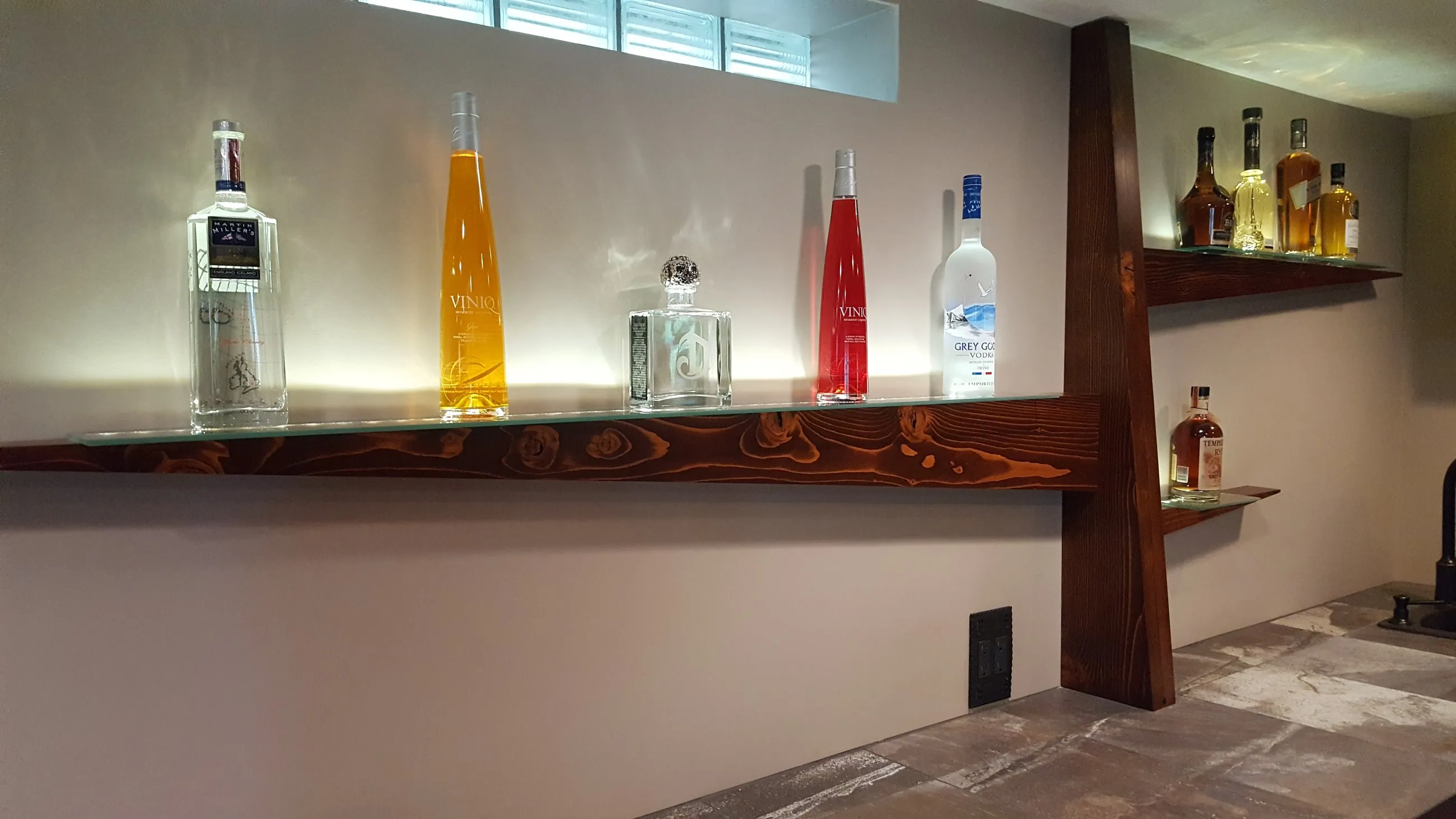 Backlit floating bottle shelf in a basement bar