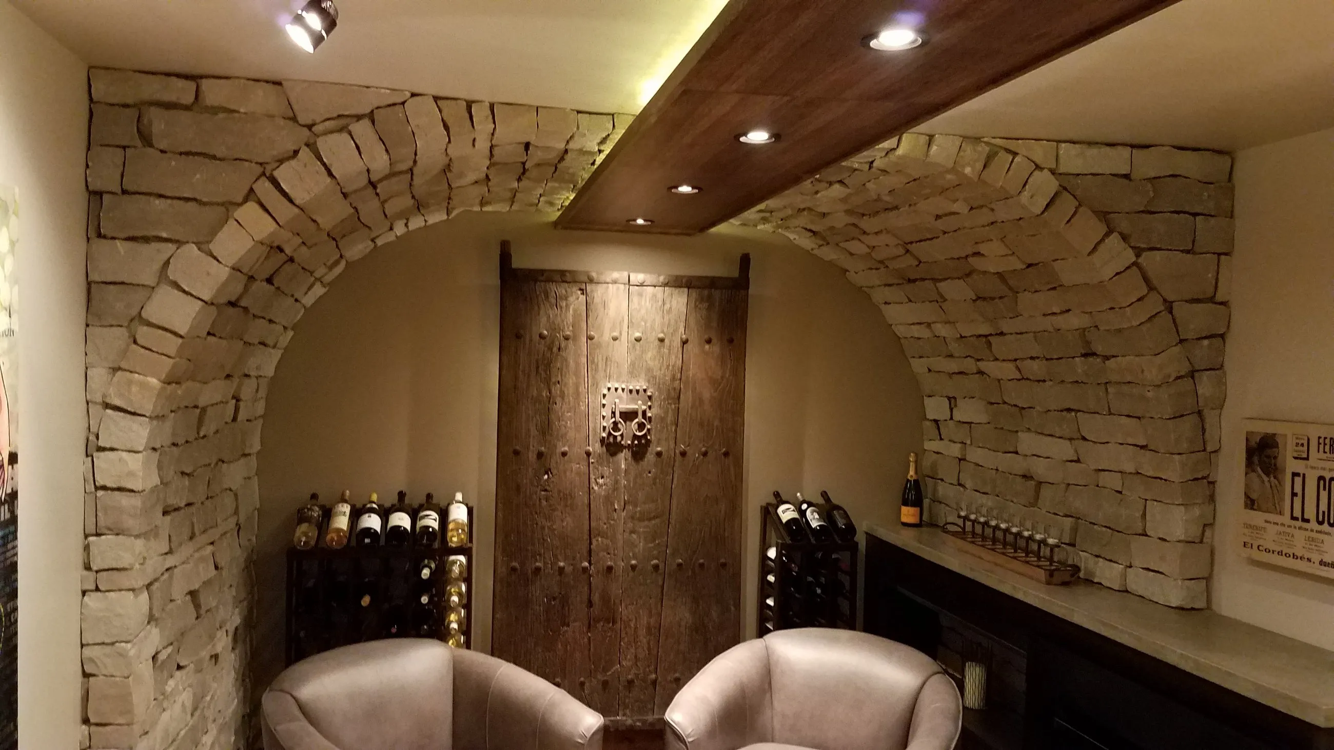 Stone barrel-vault wine room with a rustic plank door and leather club chairs