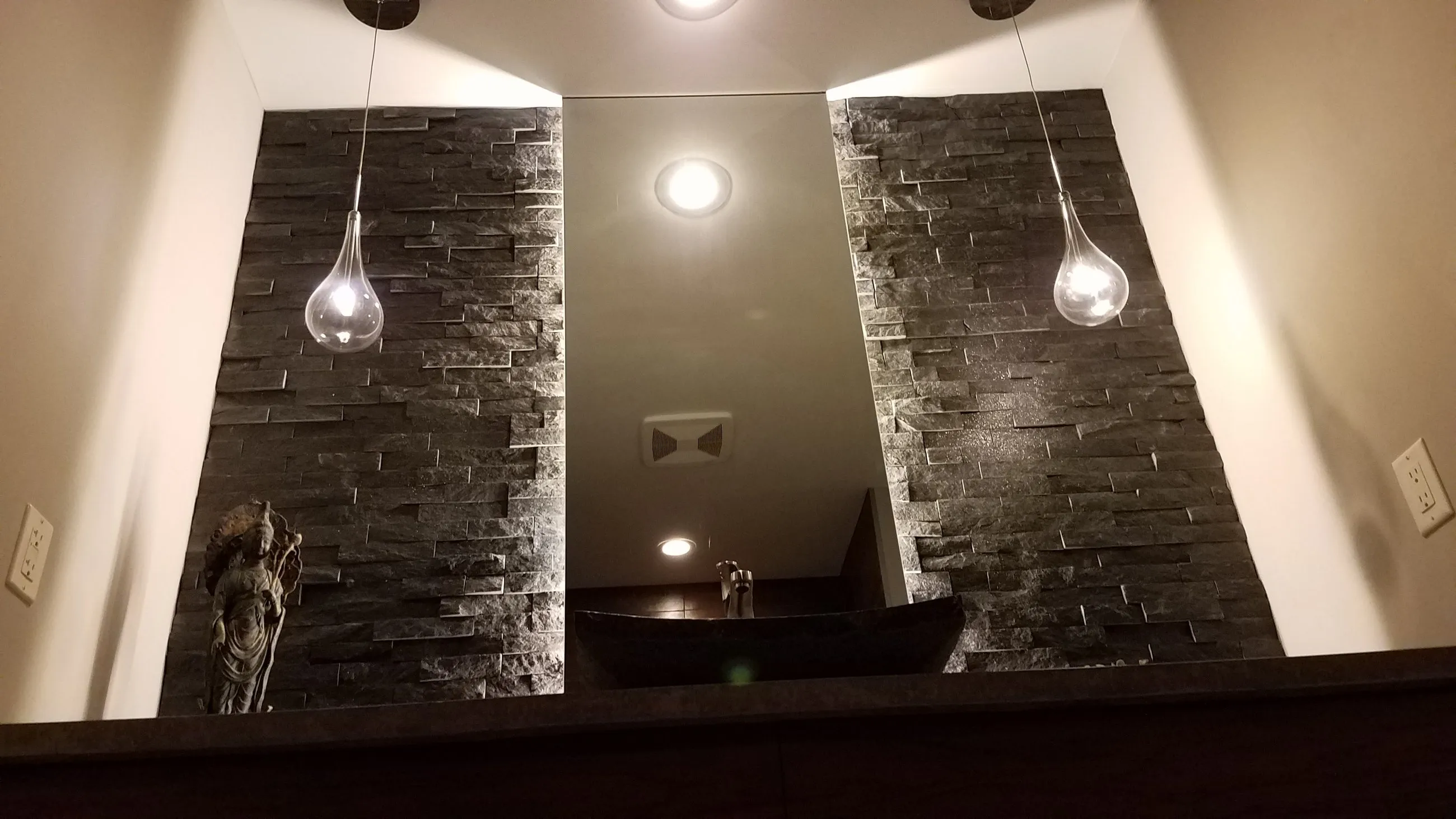 Floating dark wood vanity between stacked stone columns, with teardrop pendants