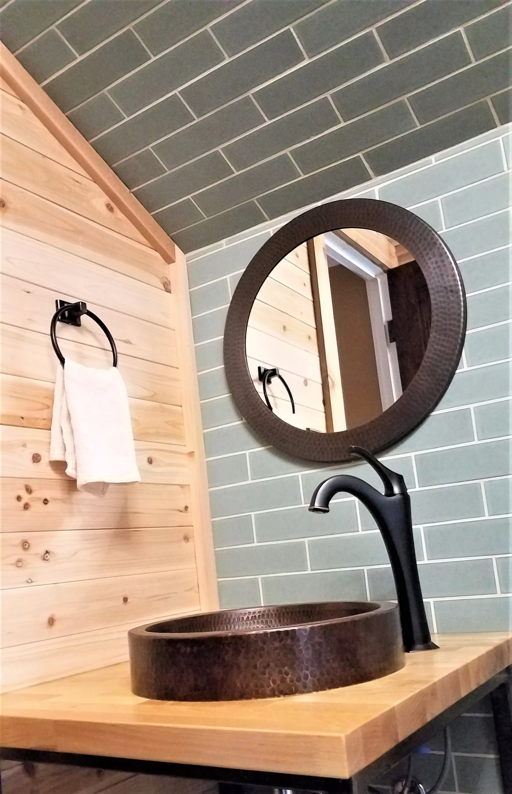 Hammered copper vessel sink on a wood and steel vanity, with knotty pine walls and sage subway tile