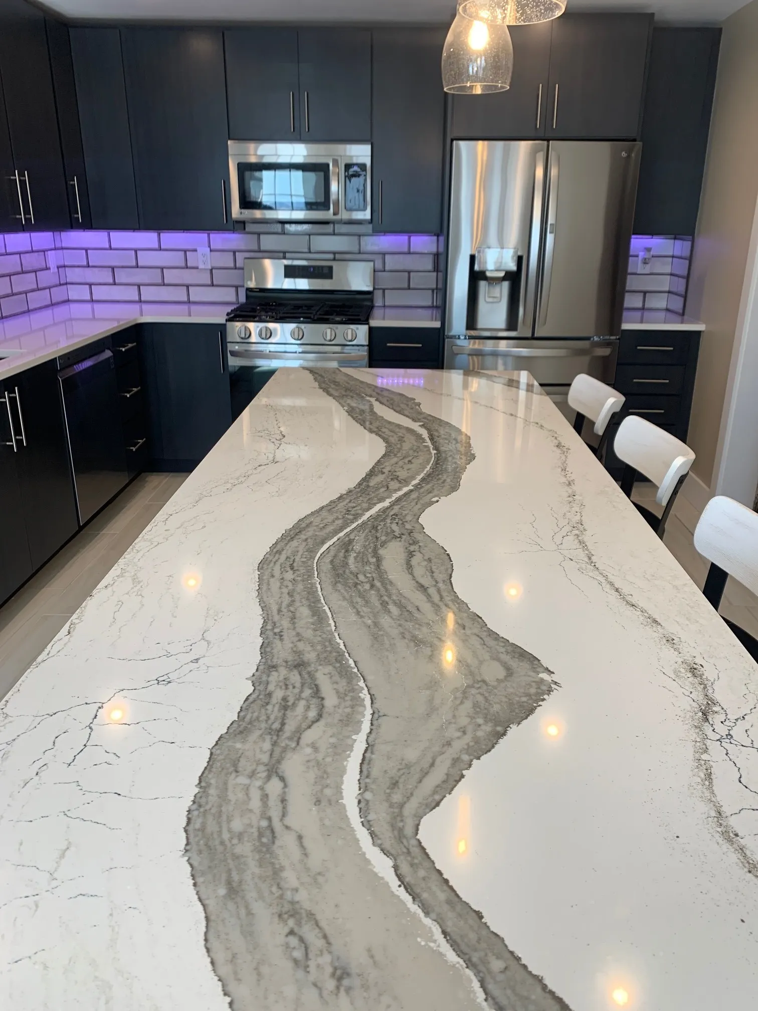 Dramatic veined-quartz waterfall island with illuminated backsplash