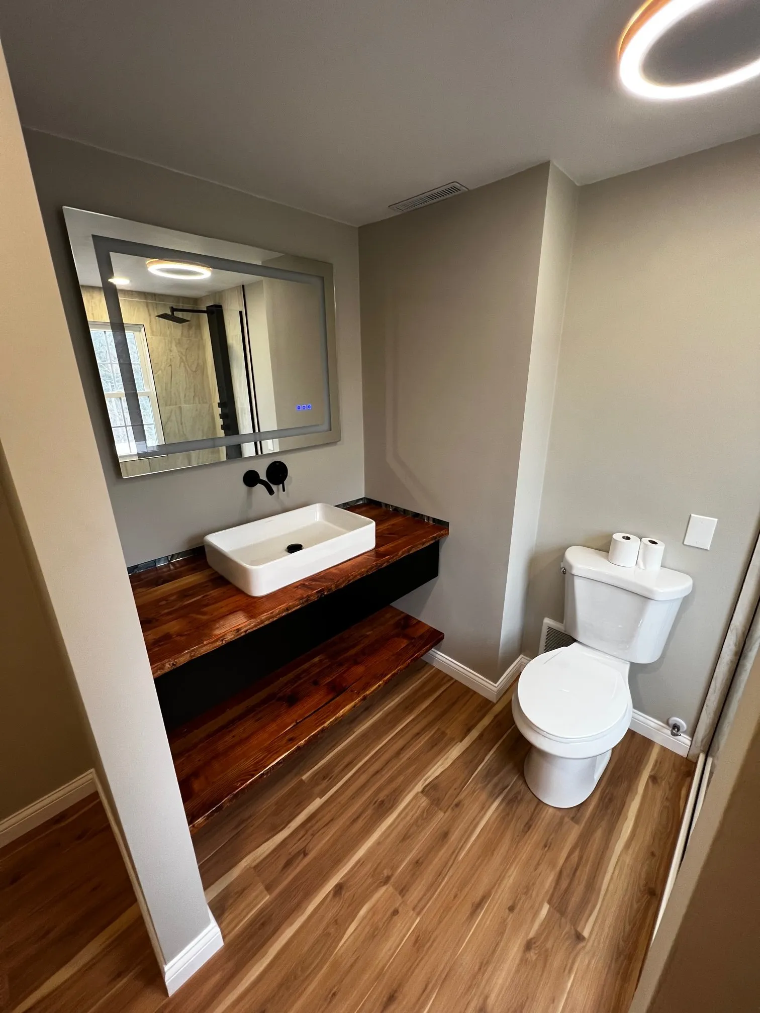 Live-edge floating vanity and toilet under a lighted mirror