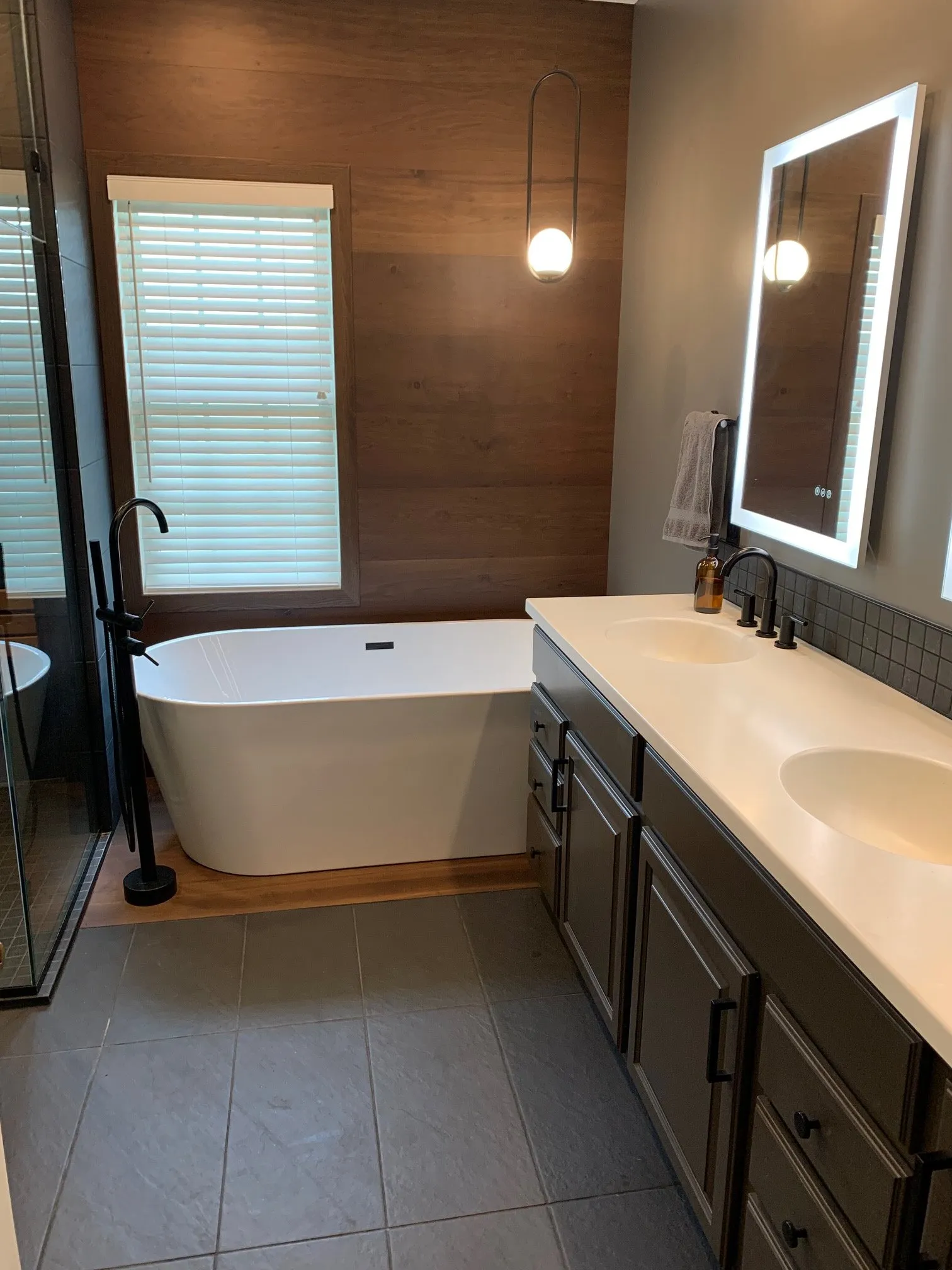 Dark wood wall, lighted mirror, and long white vanity