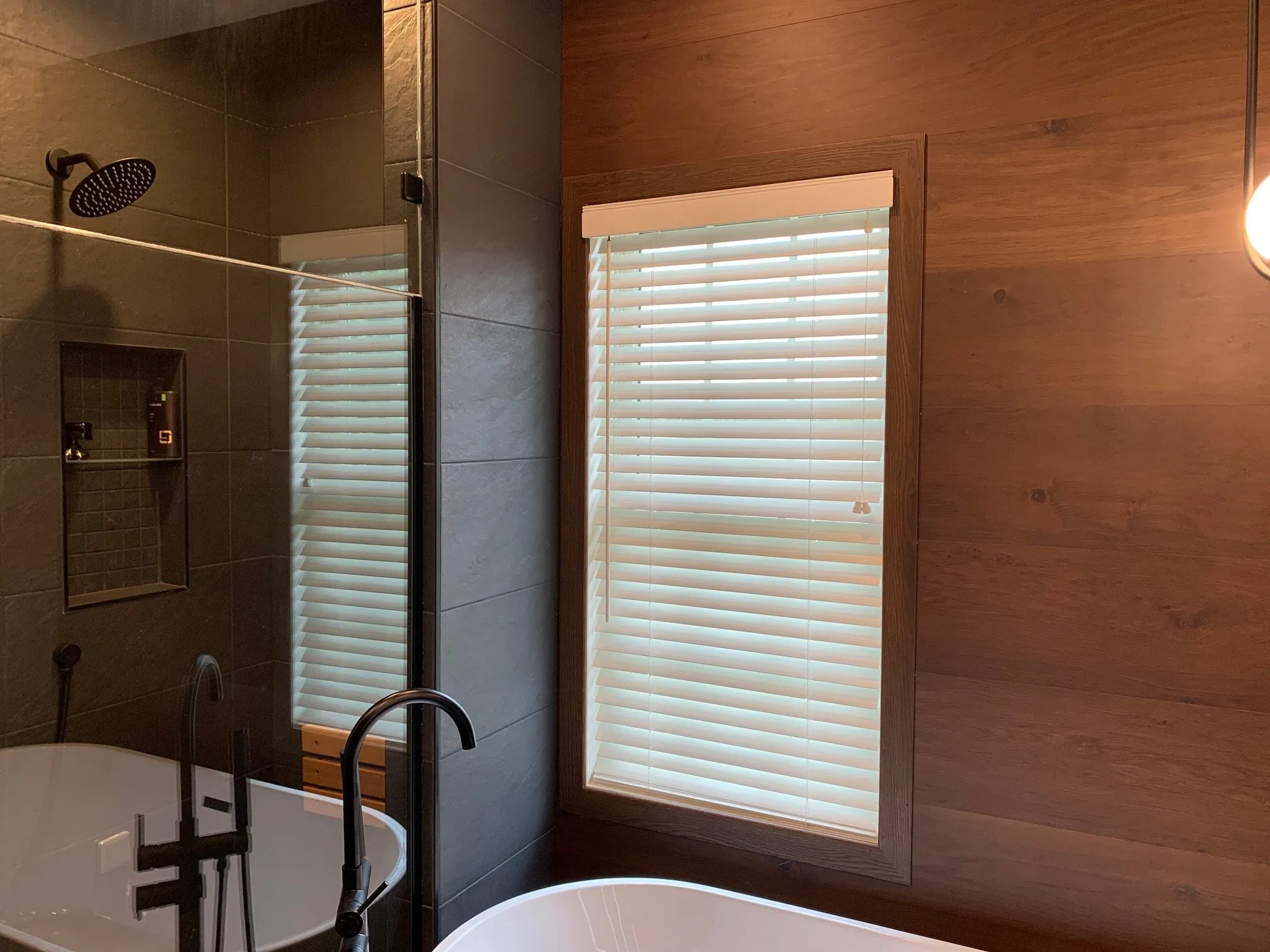 Freestanding tub beside a dark wood feature wall