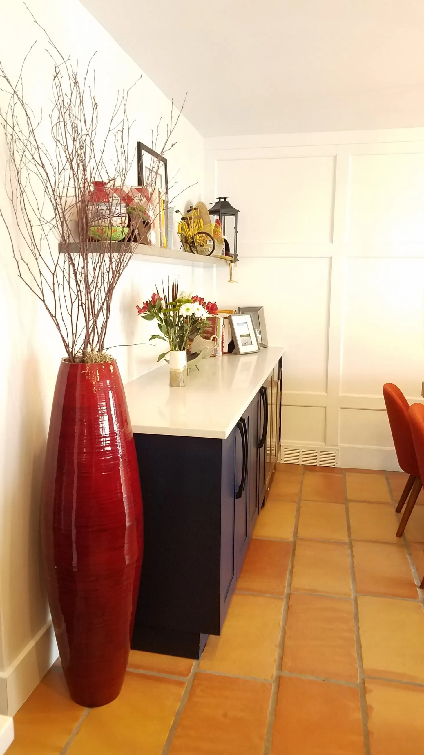 Tall red vase beside navy buffet cabinetry