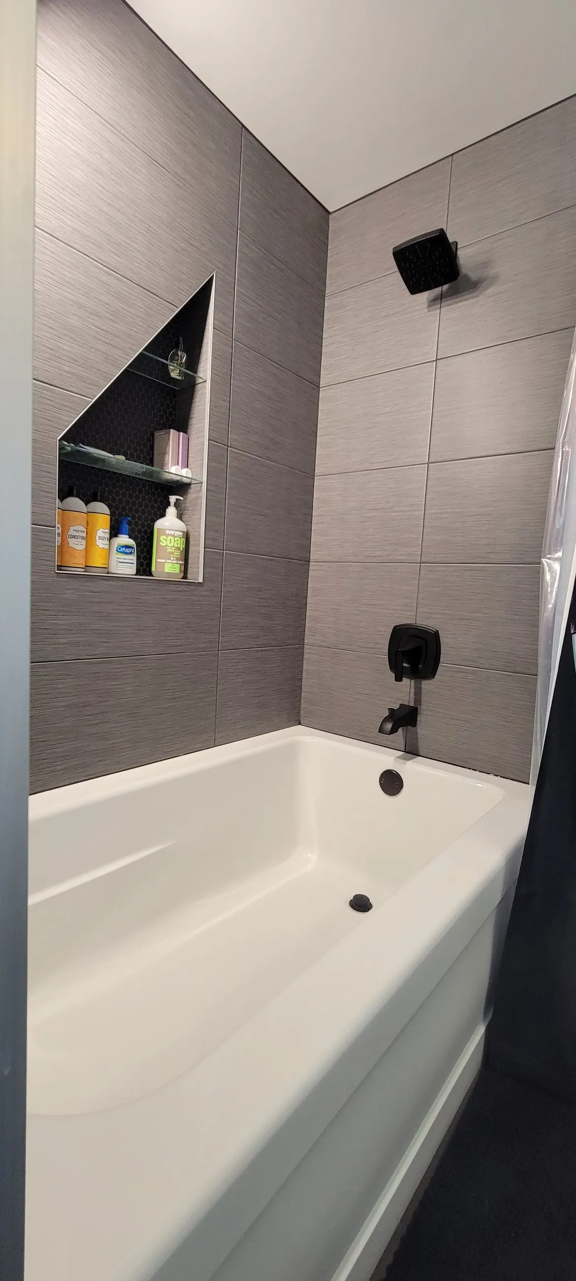 White tub with grey tile surround and angled niche