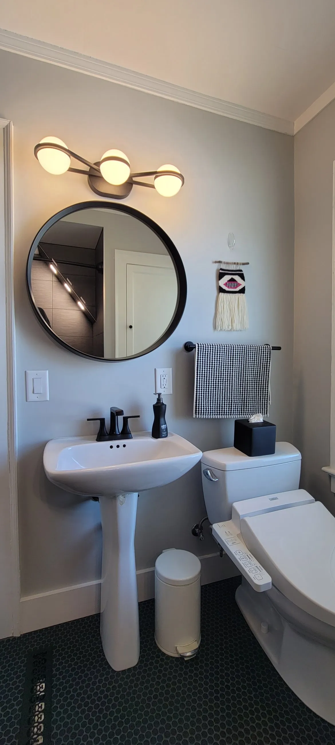 Pedestal sink, round mirror, and dark floor