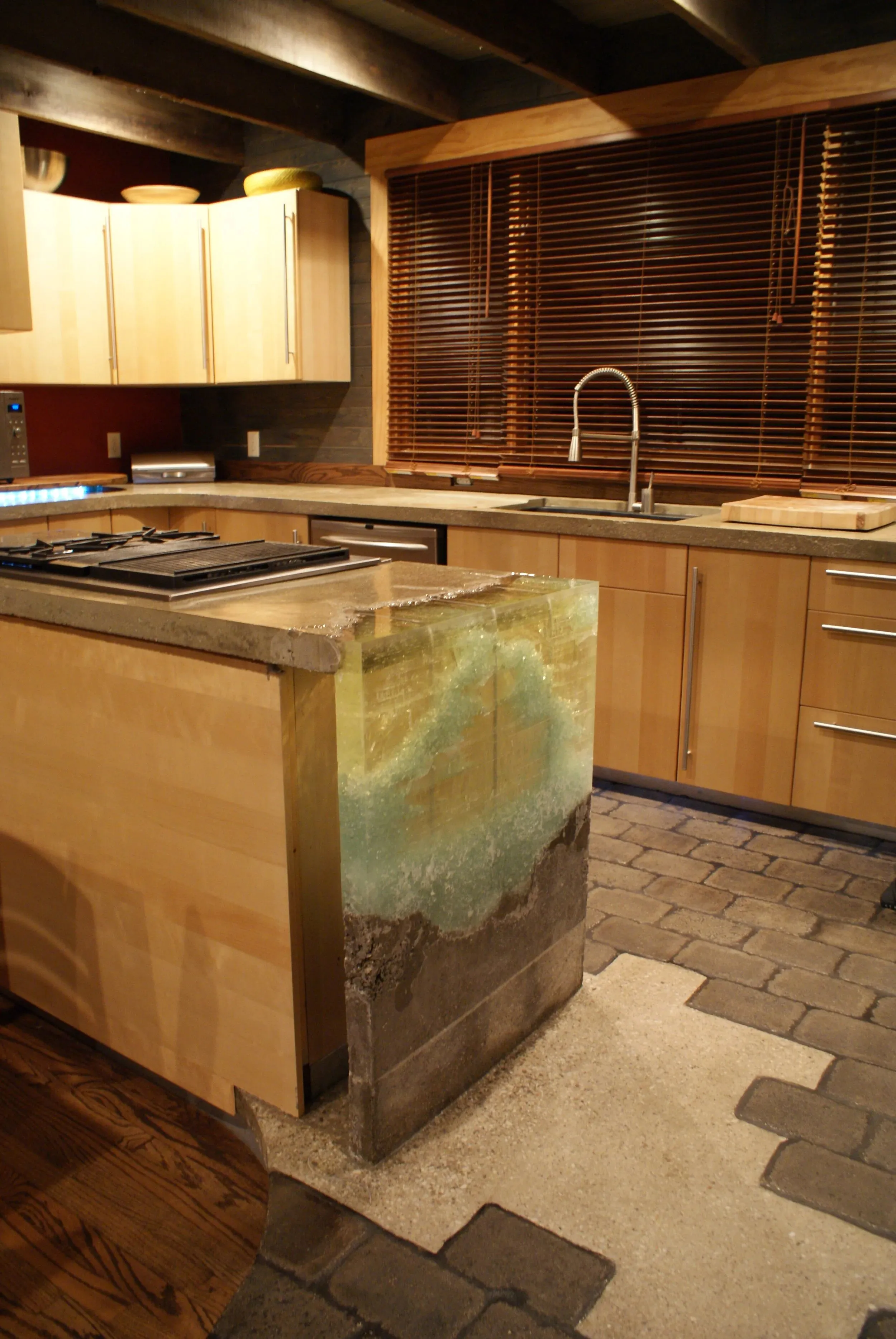 Island clad in patinated metal beside warm wood cabinetry