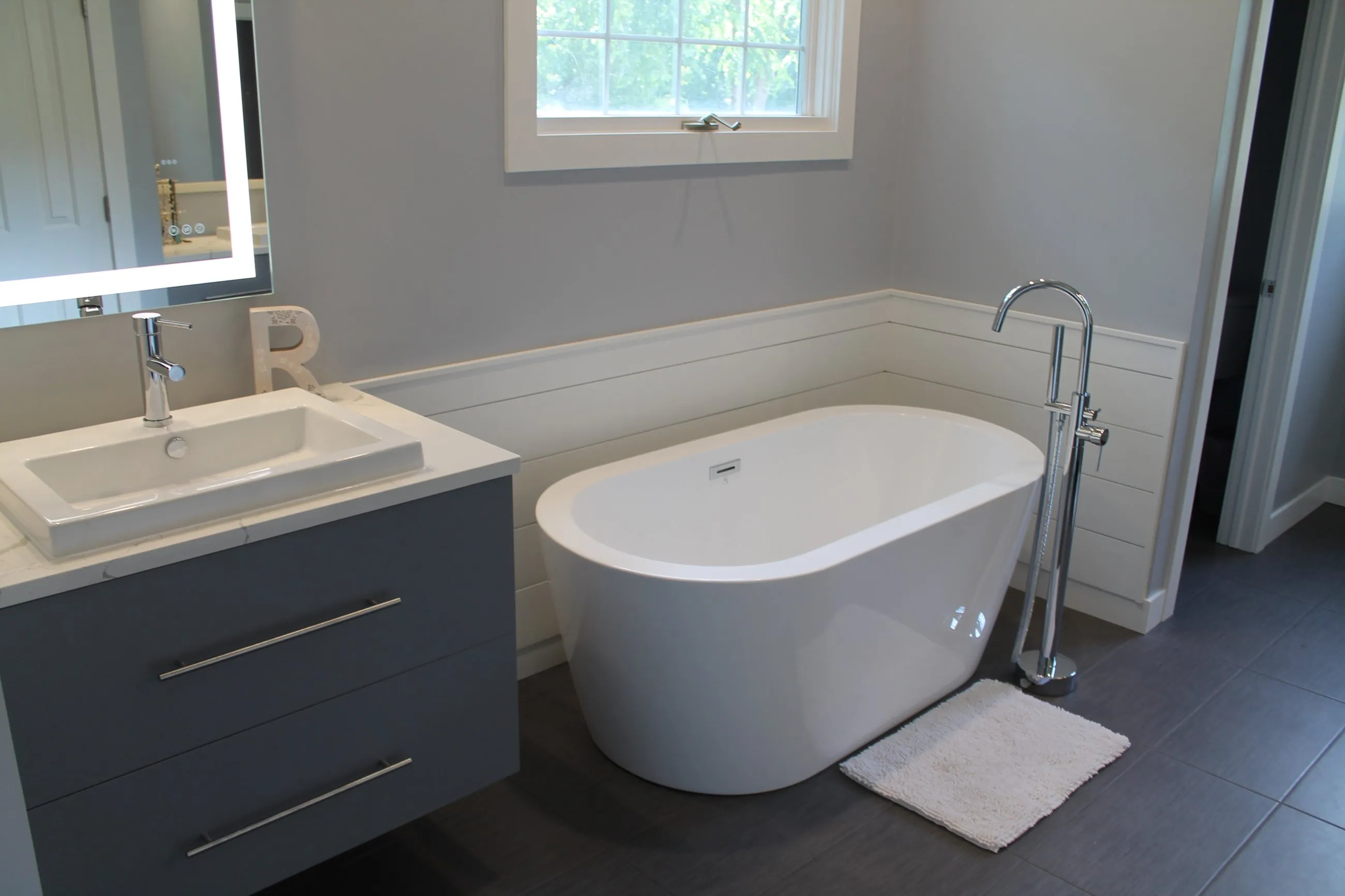 Grey floating vanity and freestanding tub under the window